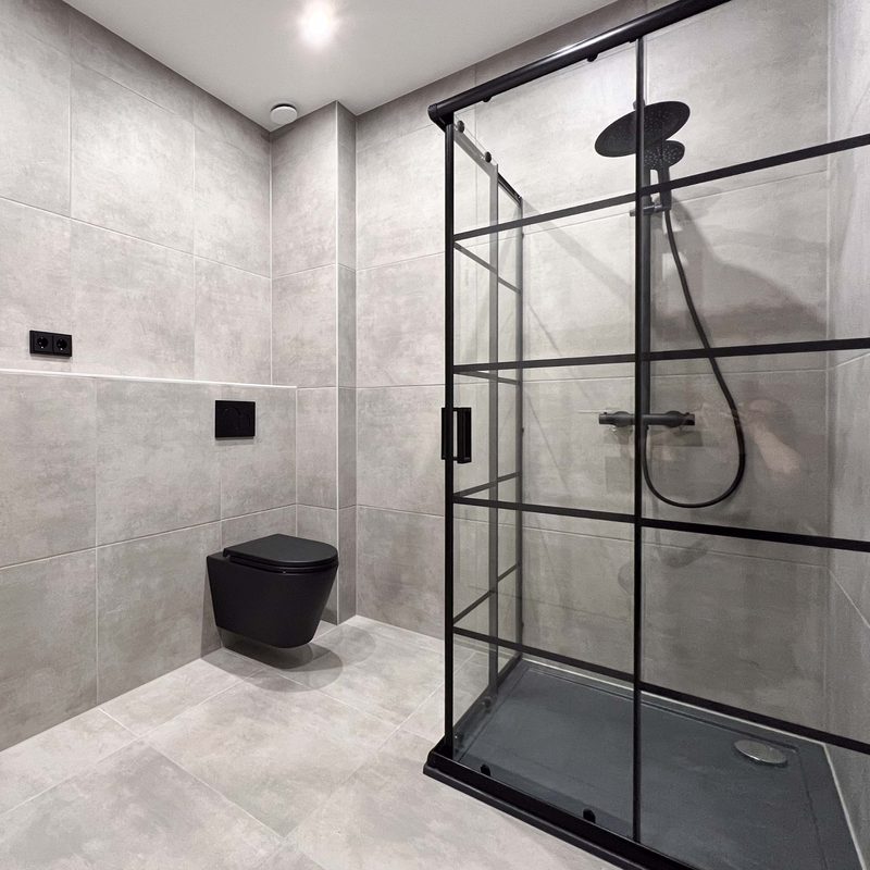 Badezimmer in Betonoptik mit schwarzer Duschabtrennung und schwarzem Wand-WC